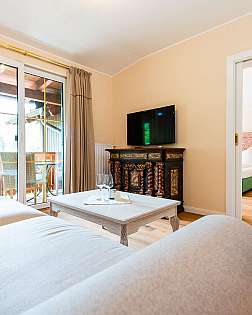 Helles Schlafzimmer mit großem Bett, Sessel, Holzkommode und Balkonfenster.