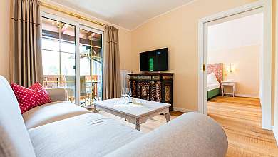 Helles Schlafzimmer mit großem Bett, Sessel, Holzkommode und Balkonfenster.