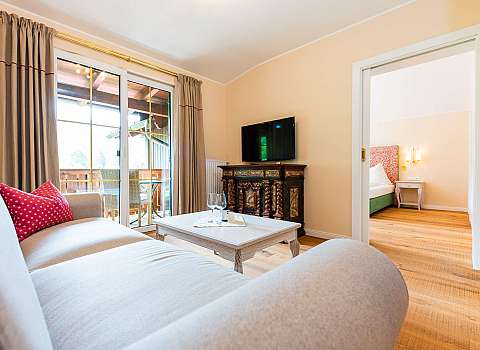 Helles Wohnzimmer mit Sofa, Fernseher, Couchtisch und Blick auf den Balkon.