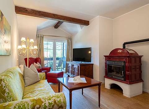 Wohnzimmer mit grünem Sofa, rotem Sessel, Fernseher und Kaminofen
