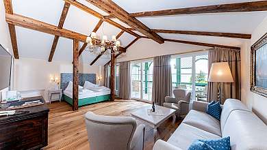 Spacious hotel room with exposed wooden beams, bed, seating area and large floor-to-ceiling windows.